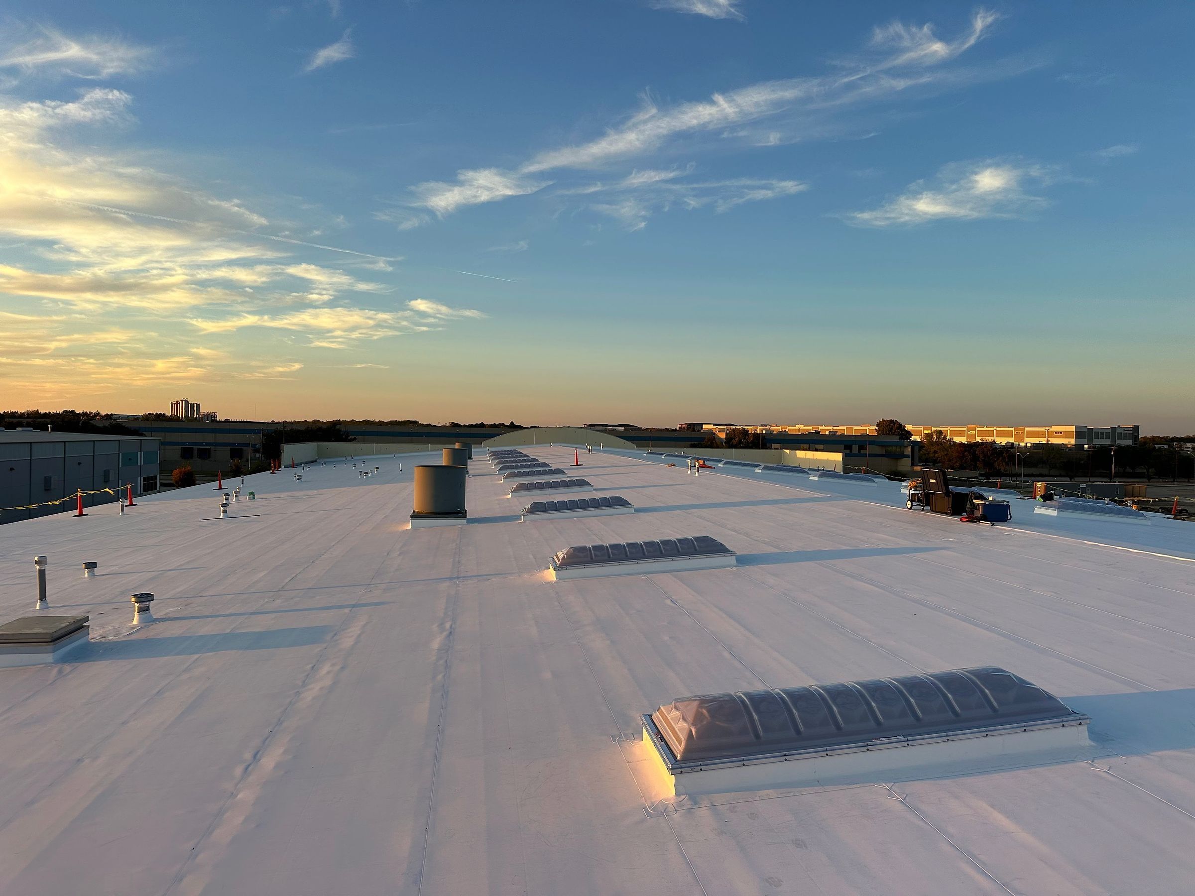 Finished white TPO membrane roof with skylights in the foreground at golden hour