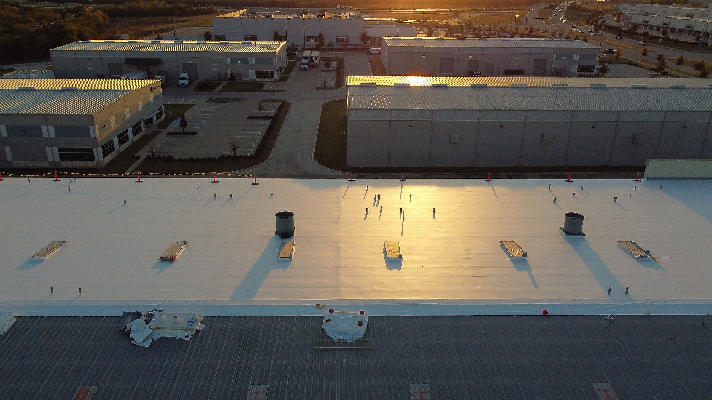 TPO retrofit over an R-panel metal roof at golden hour, new white TPO beside metal panels still to be covered, Mansfield, TX