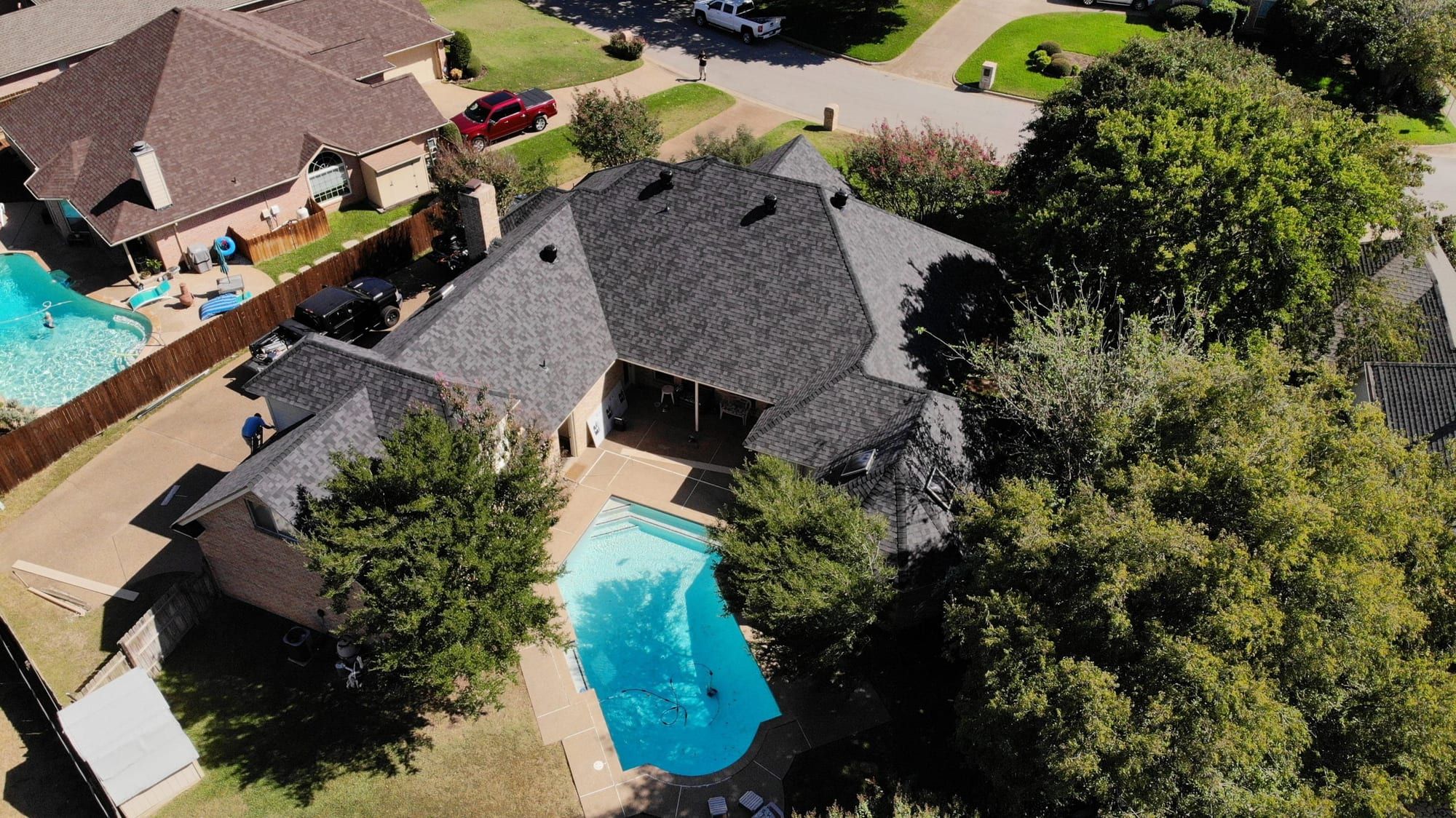Aerial view of a finished shingle roof on a two-story home with a backyard pool