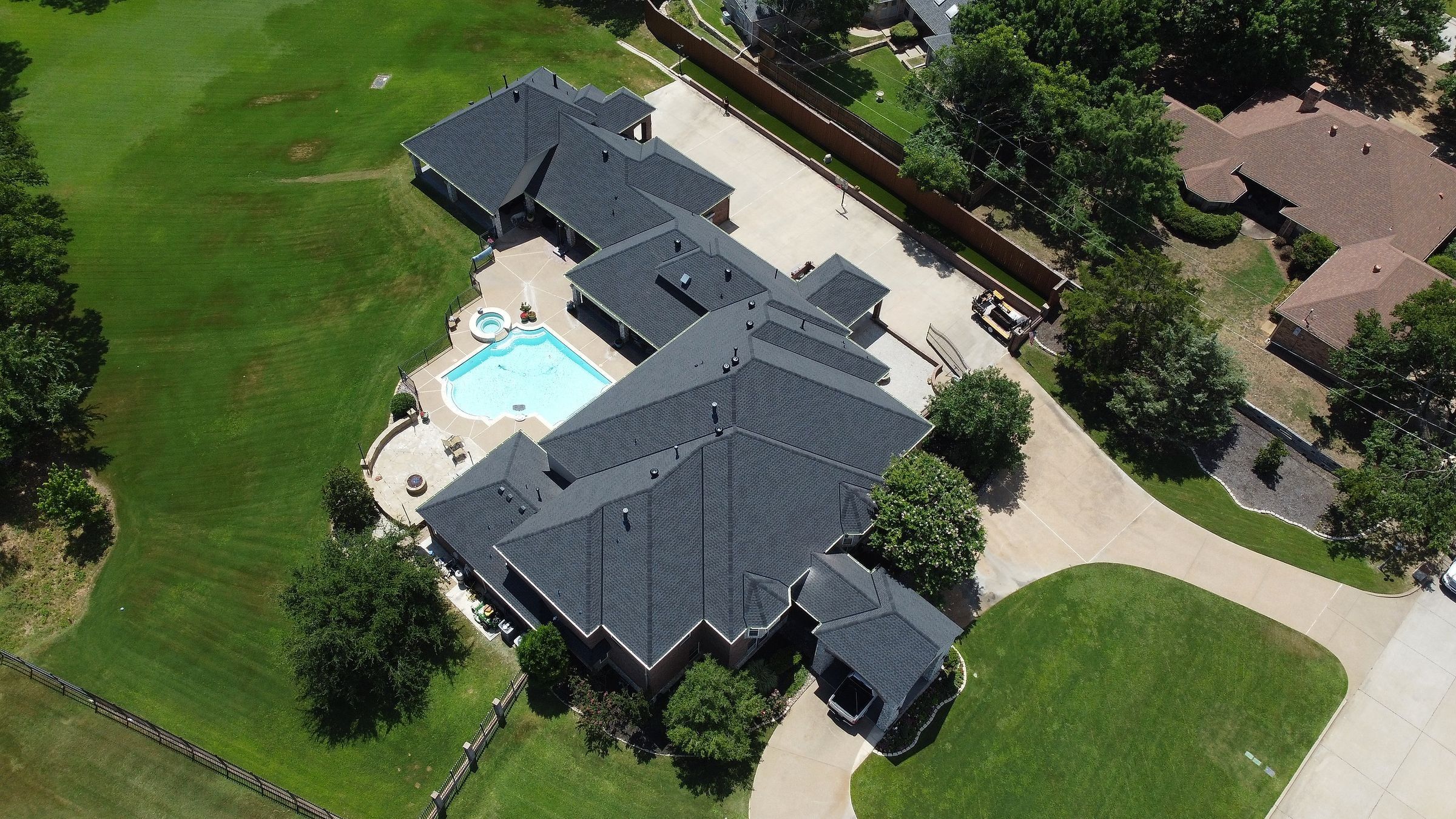 Charcoal shingle roof on a large home with a pool and curved driveway