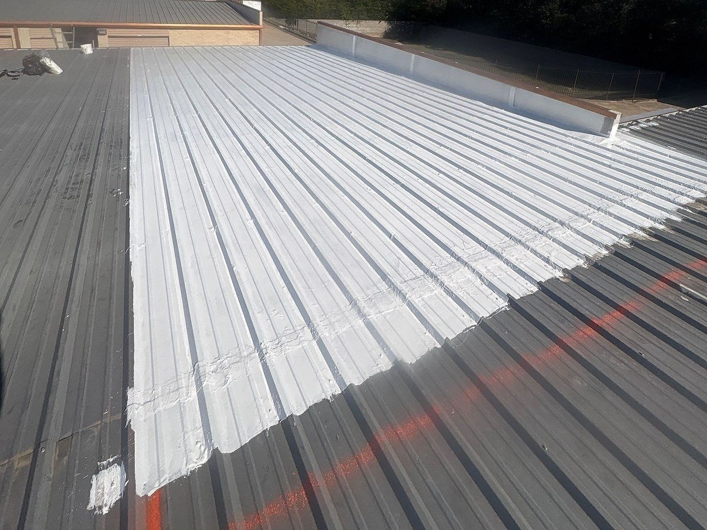White roof coating rolled over a ribbed metal roof, with uncoated panels alongside