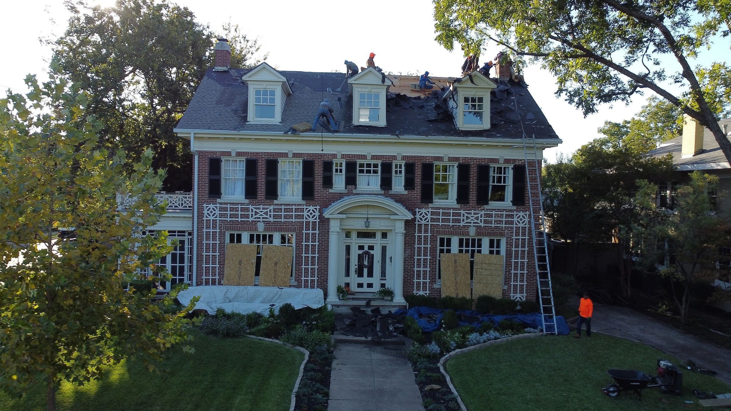 Crew on the roof of a two-story brick colonial home in Dallas, TX, plywood over the windows