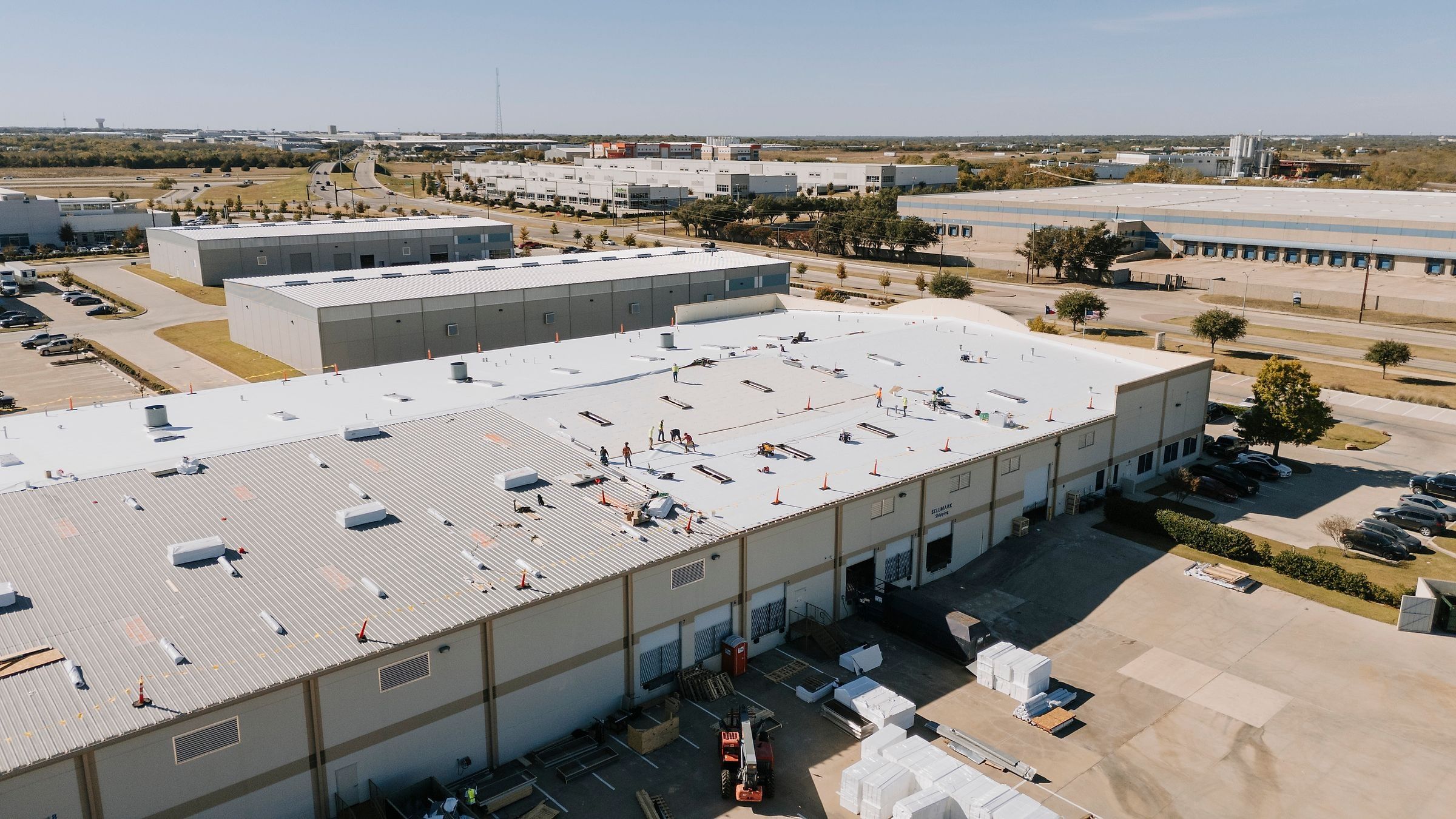 Crew installing a white TPO roof over the old metal roof of a Mansfield, TX warehouse, seen from a drone