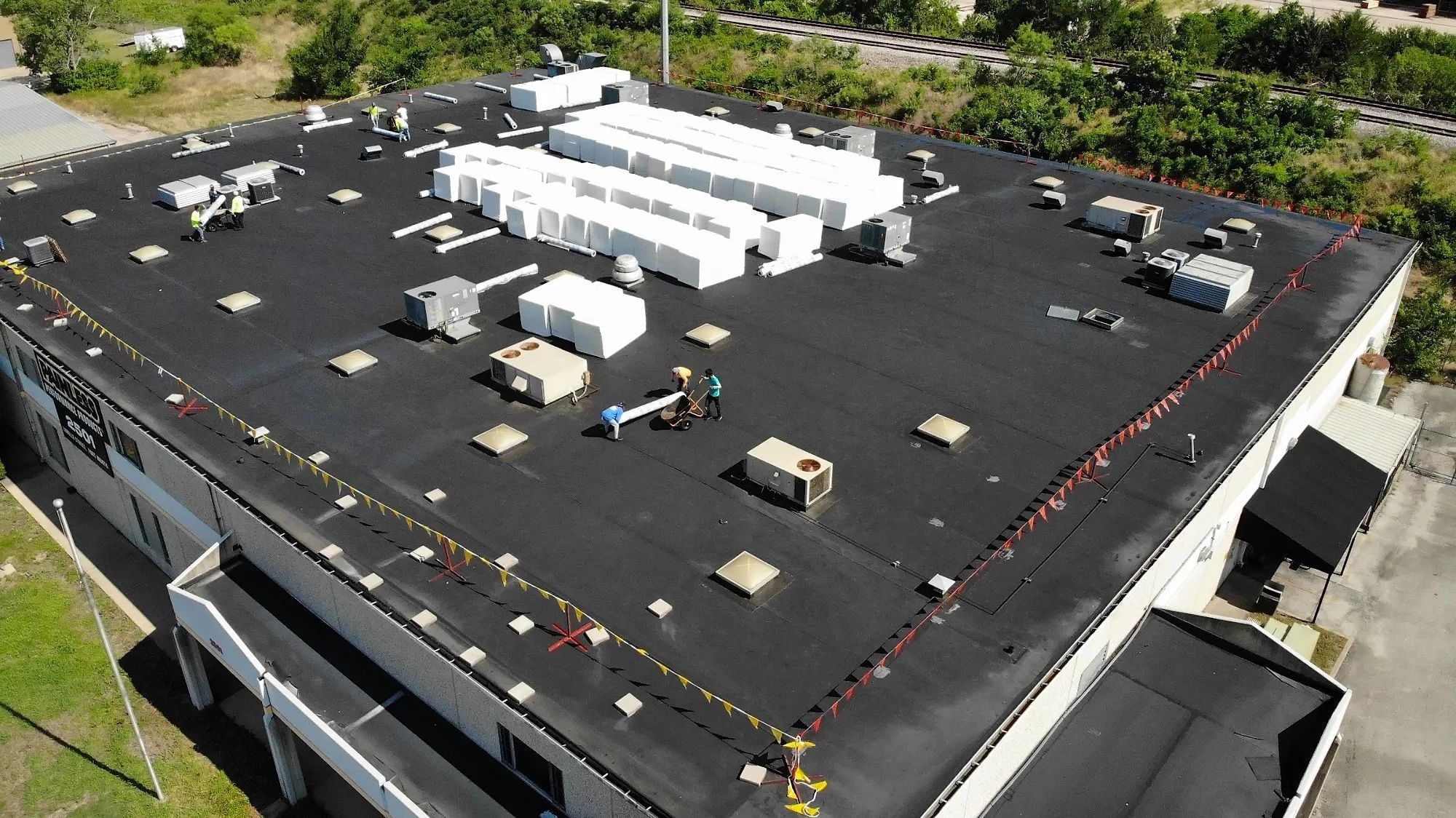 Crew working on a black EPDM roof on a commercial building, with insulation board staged across the roof, seen from a drone