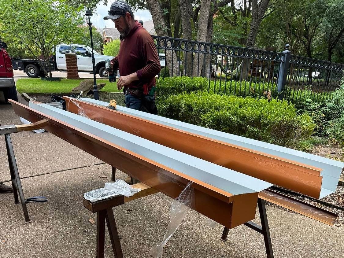 Roofer assembling new copper-colored metal gutters on sawhorses in a driveway