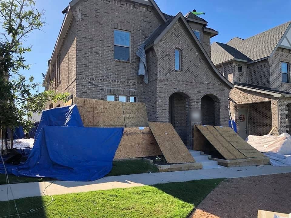 Plywood over the windows and tarps over the landscaping at a brick home