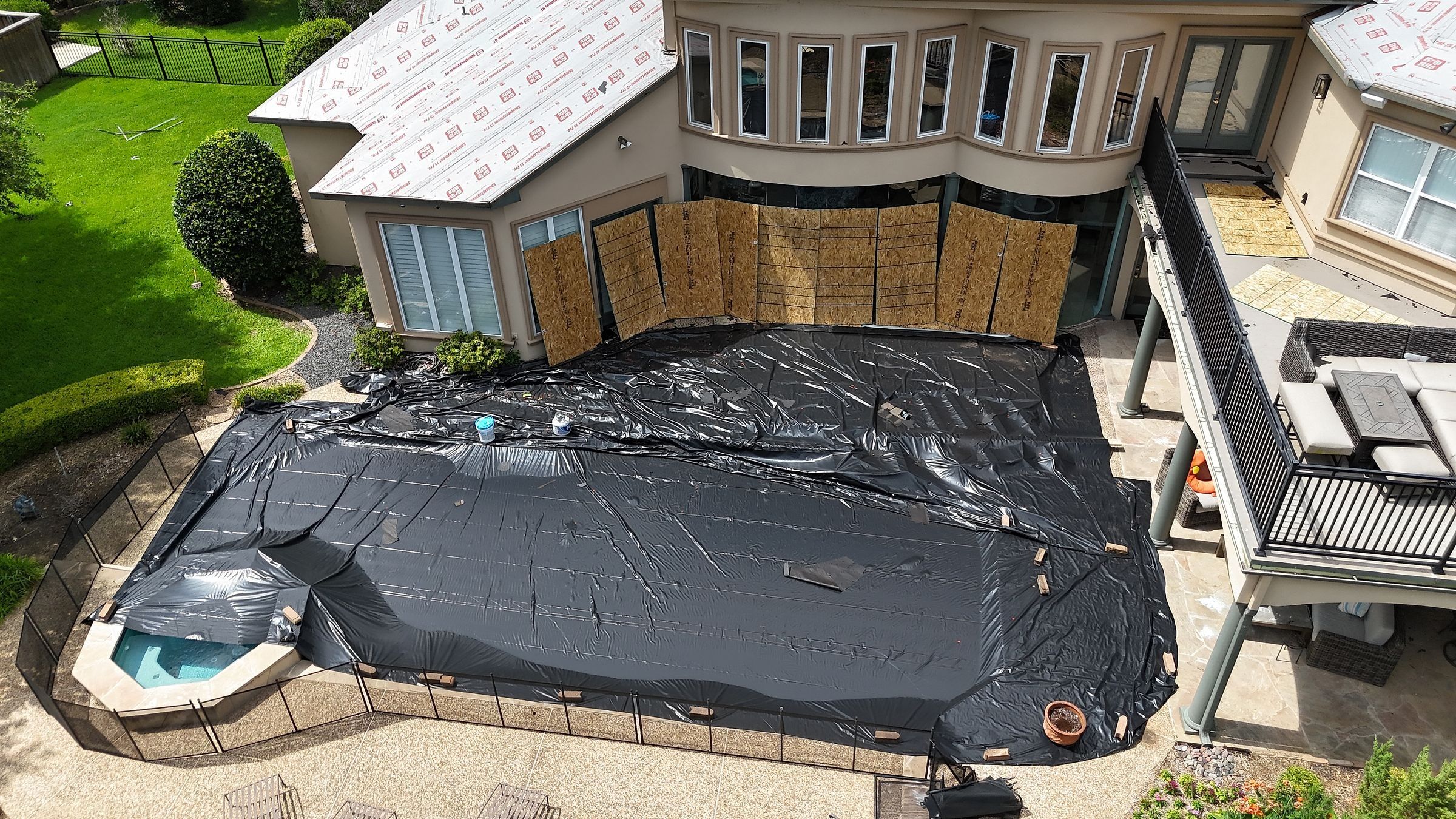 Pool covered with a black tarp and windows boarded with plywood during a roof replacement
