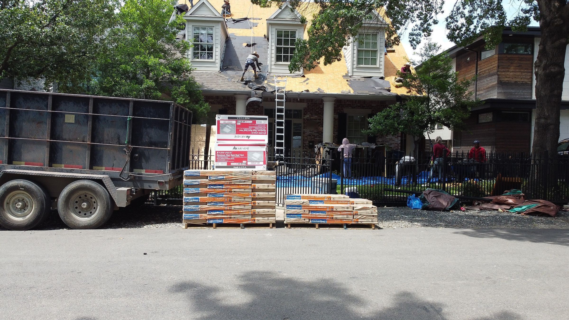 Crew on the roof of a two-story home, with new shingles and a dump trailer out front