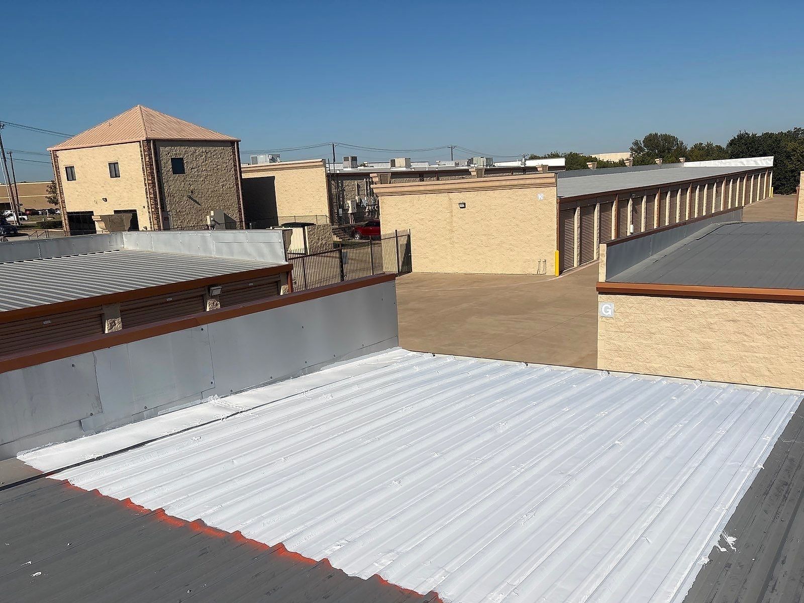 White silicone roof coating applied over part of a gray metal roof on a commercial building