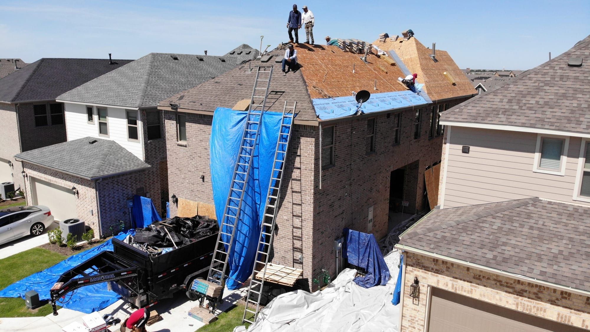 Crew on the roof of a two-story home with a tarp over the damaged section