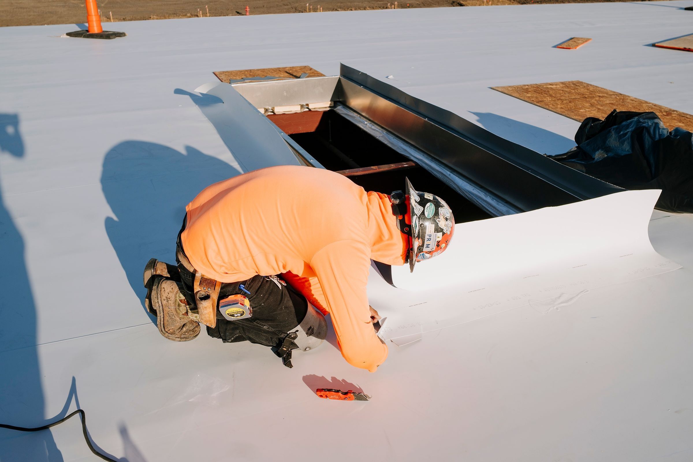 Roofer wrapping TPO membrane up the side of a skylight curb