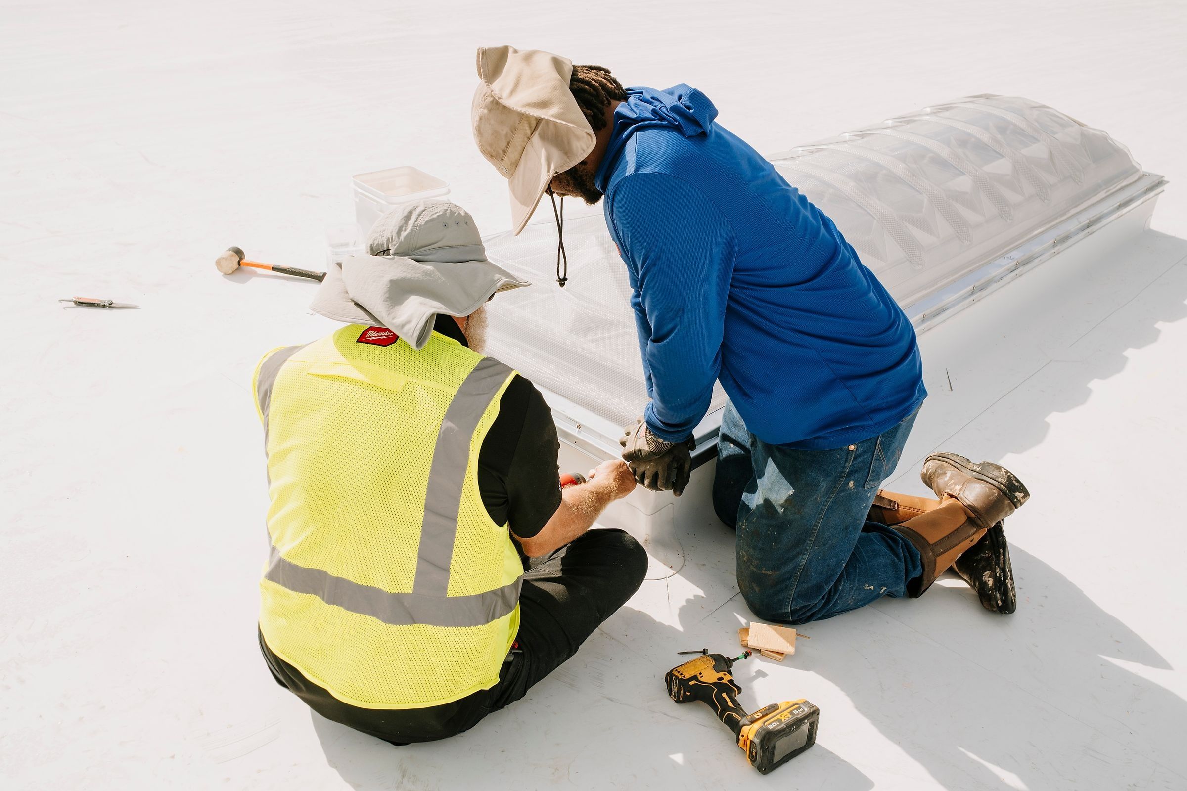 Two roofers fastening a skylight dome to its curb