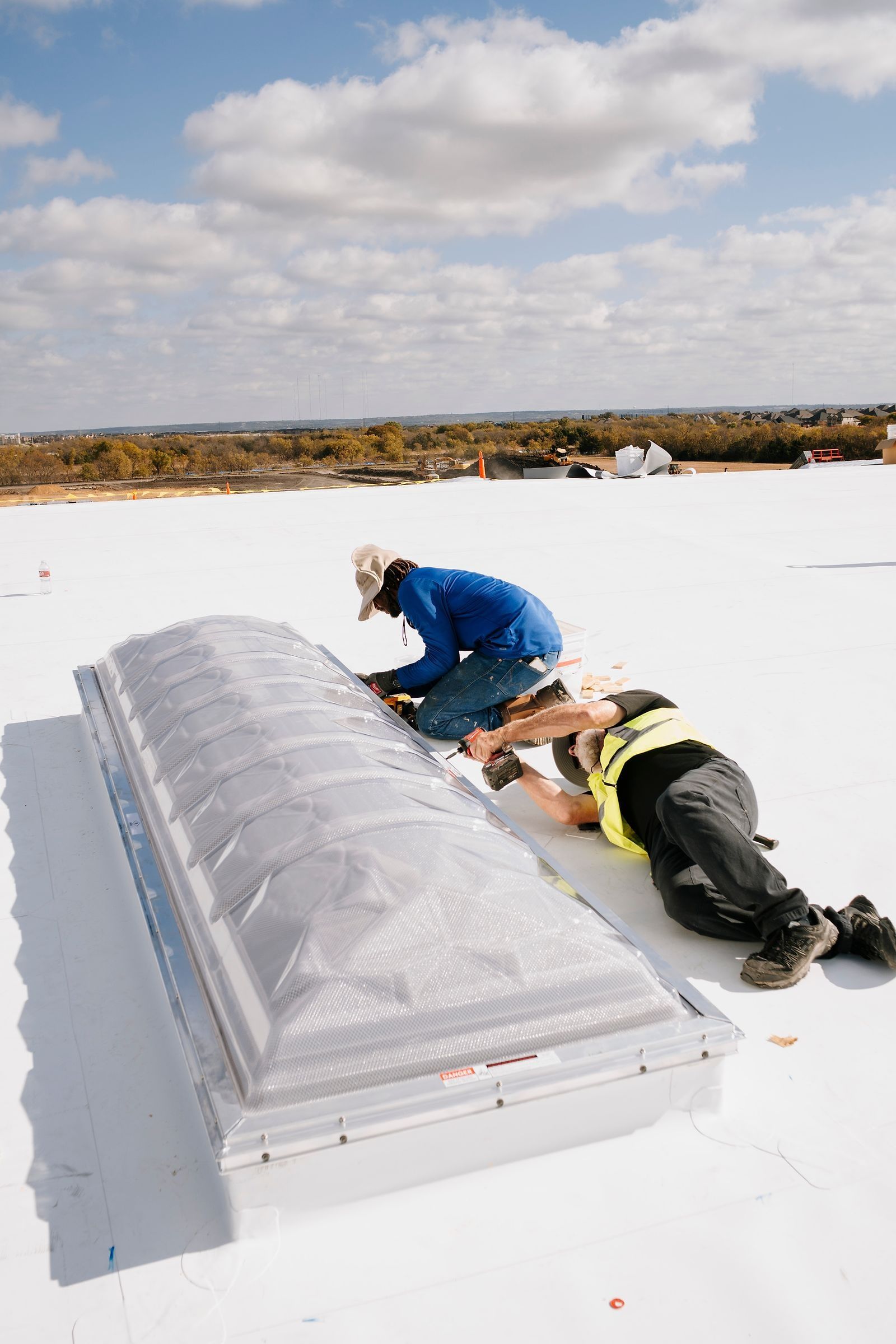 Roofers securing a skylight dome on a white TPO roof