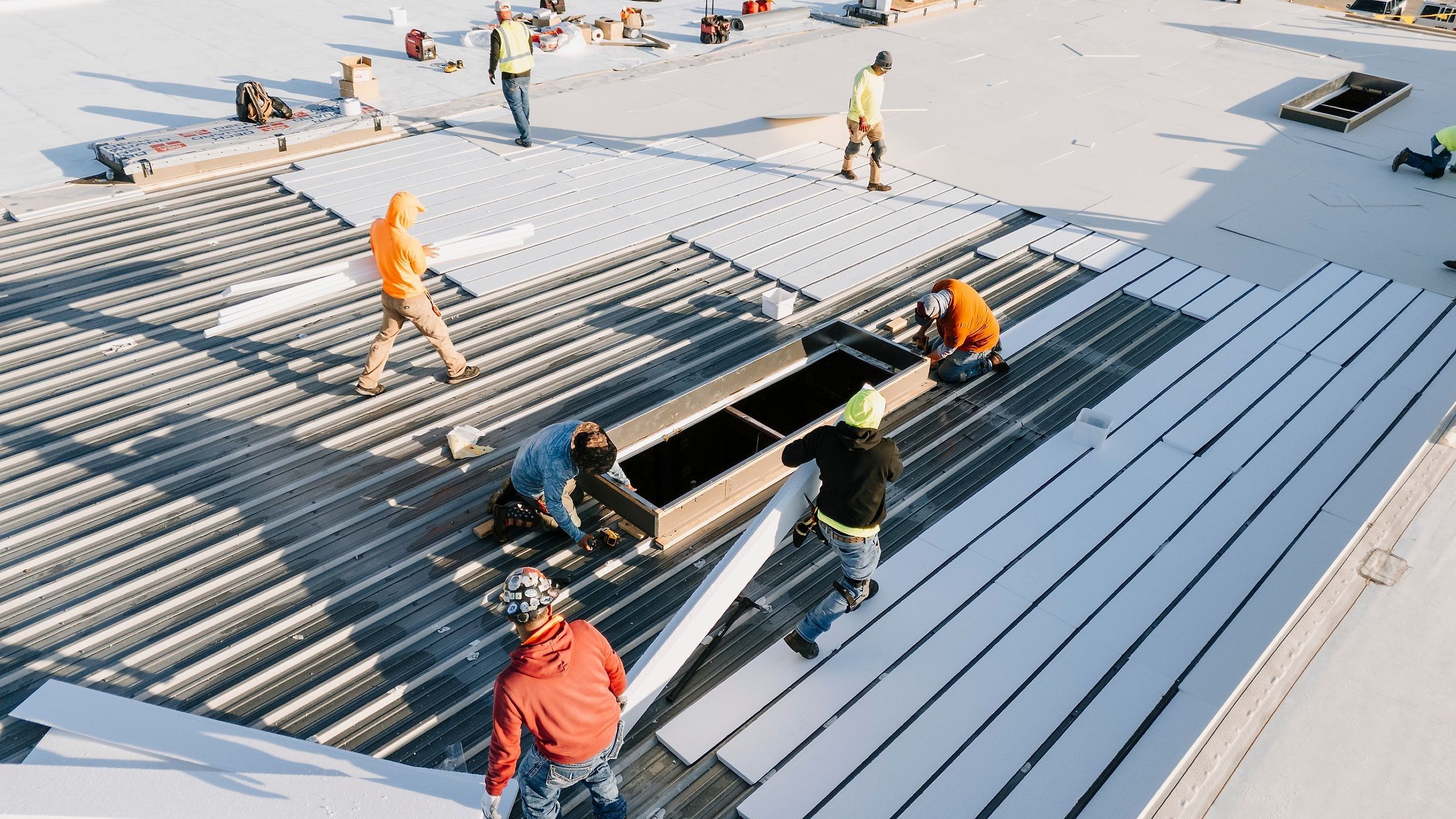Crew laying insulation board over a ribbed metal warehouse roof