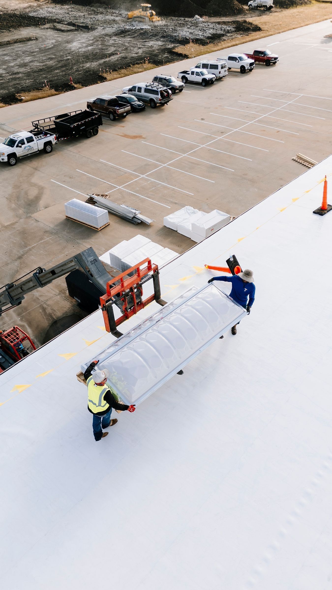 Telehandler lifting a skylight onto a white TPO roof